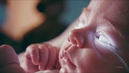 Close-up of a newborn baby with bright, glowing eyes, resting peacefully.